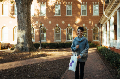 Student holding tote bag with purple Scottie walking beside Rebekah Hall