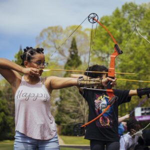 Students in a line aim at a target with a bow and arrowl
