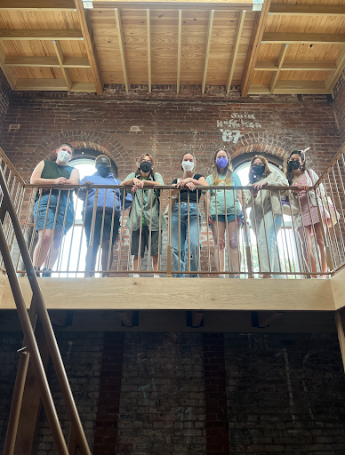 Seven students, wearing face masks, look down at the camera from a balcony