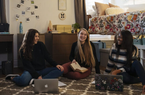 Three students sitting in a dorm room looking at laptops