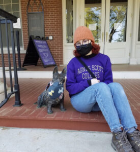 Lily Grosshans wearing an Agnes Scott shirt and a facemask seated next to Ramona, a Scottie dog statue