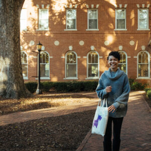 Student holding tote bag with purple Scottie walking beside Rebekah Hall