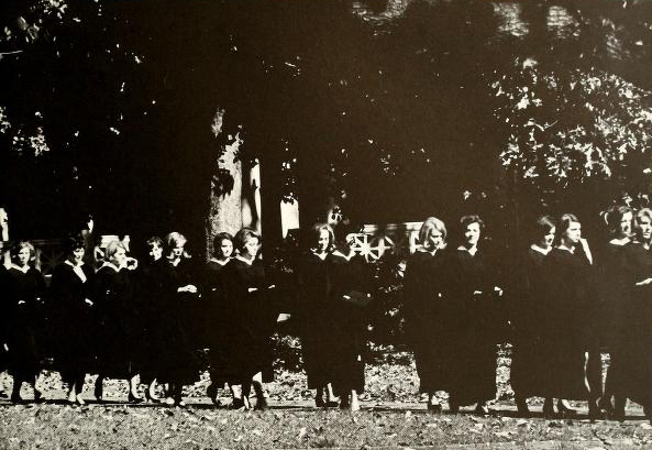 Black and white photo of students in commencement gowns running across campus.