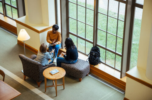 Three Agnes Scott students chat over books in the library.