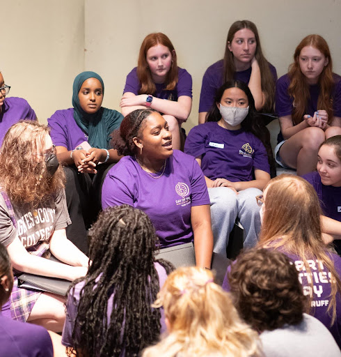 Students in a group listed to student in purple tee-shirt talk.