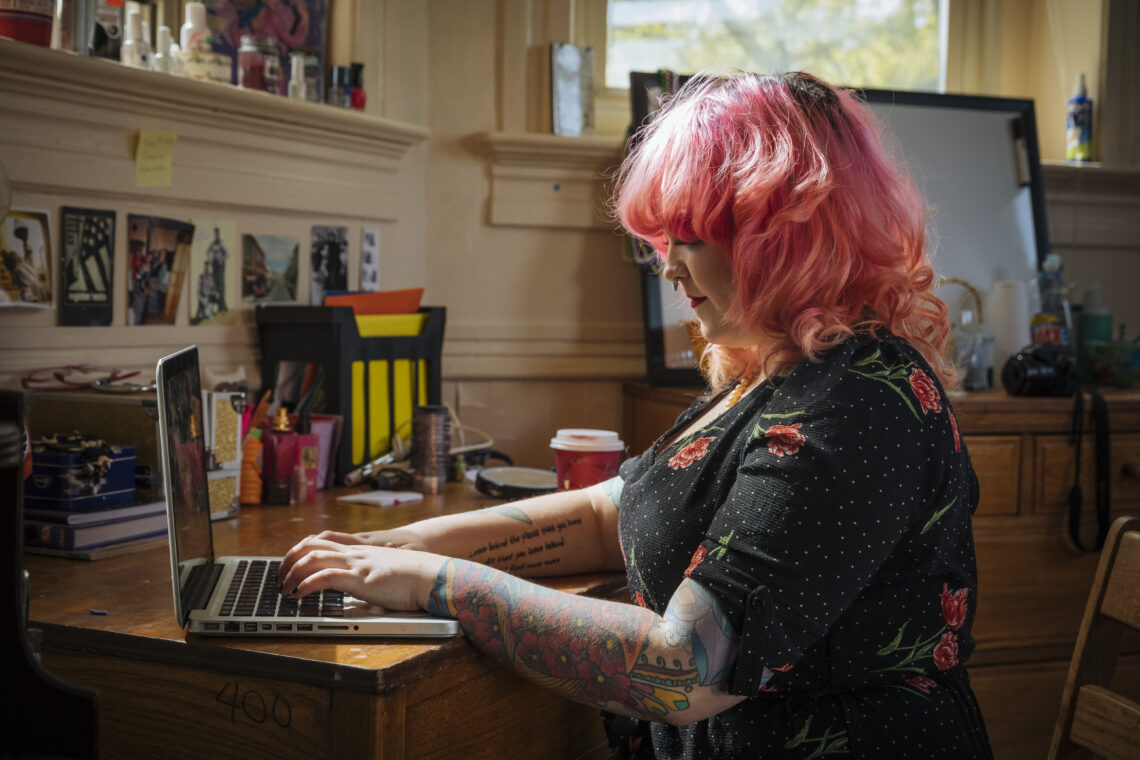 Student with pink hair types an essay on her laptop.