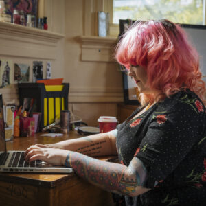Student with pink hair types an essay on her laptop.